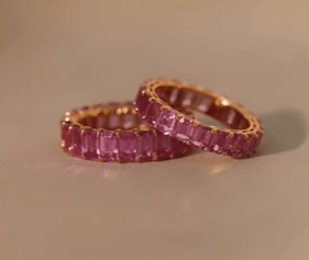 A woman wears two emerald cut pink sapphire eternity bands in rose gold.