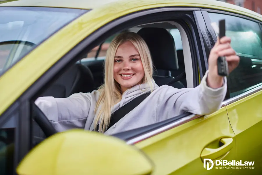 smiling teen driving a green car showing off her keys with her hand out the window