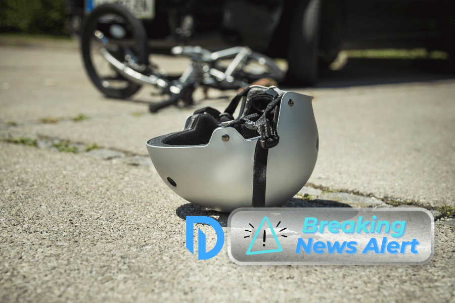 helmet laying on the road beside a bike accident. "Breaking News Alert" badge overlay in the corner