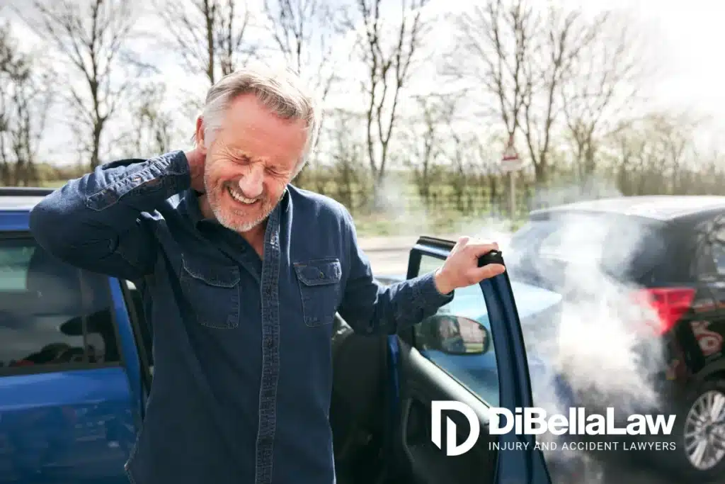 A man rubbing his neck stepping out of a car that is crashed into another car