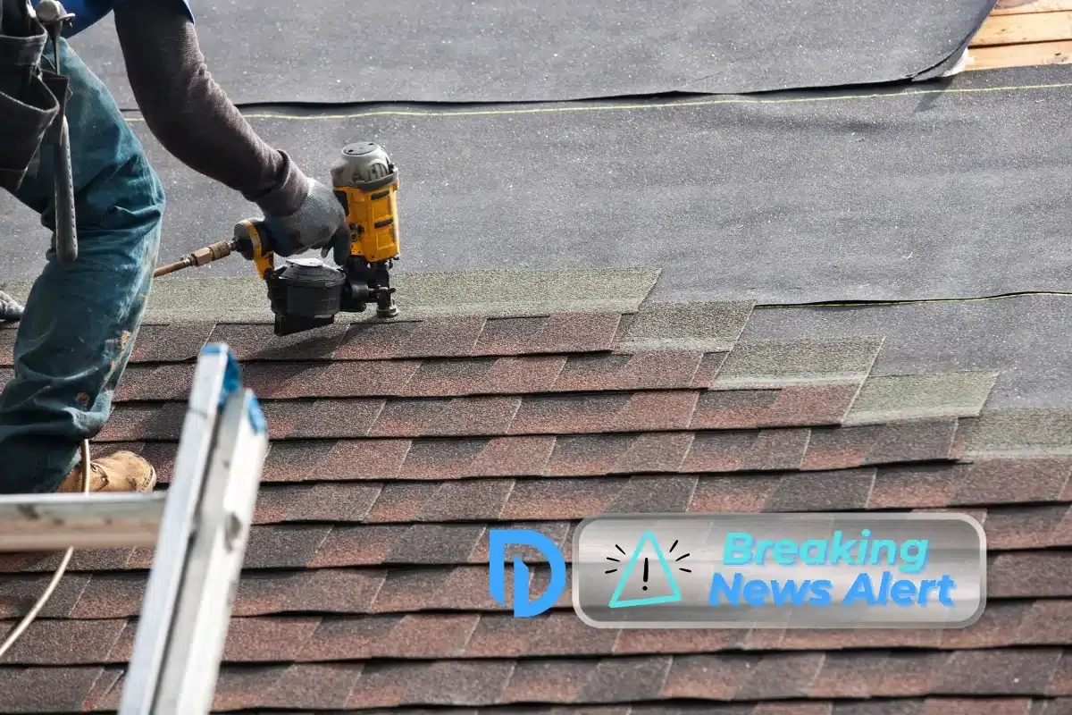 A construction worker on a ladder nailing roofing shingles into place.