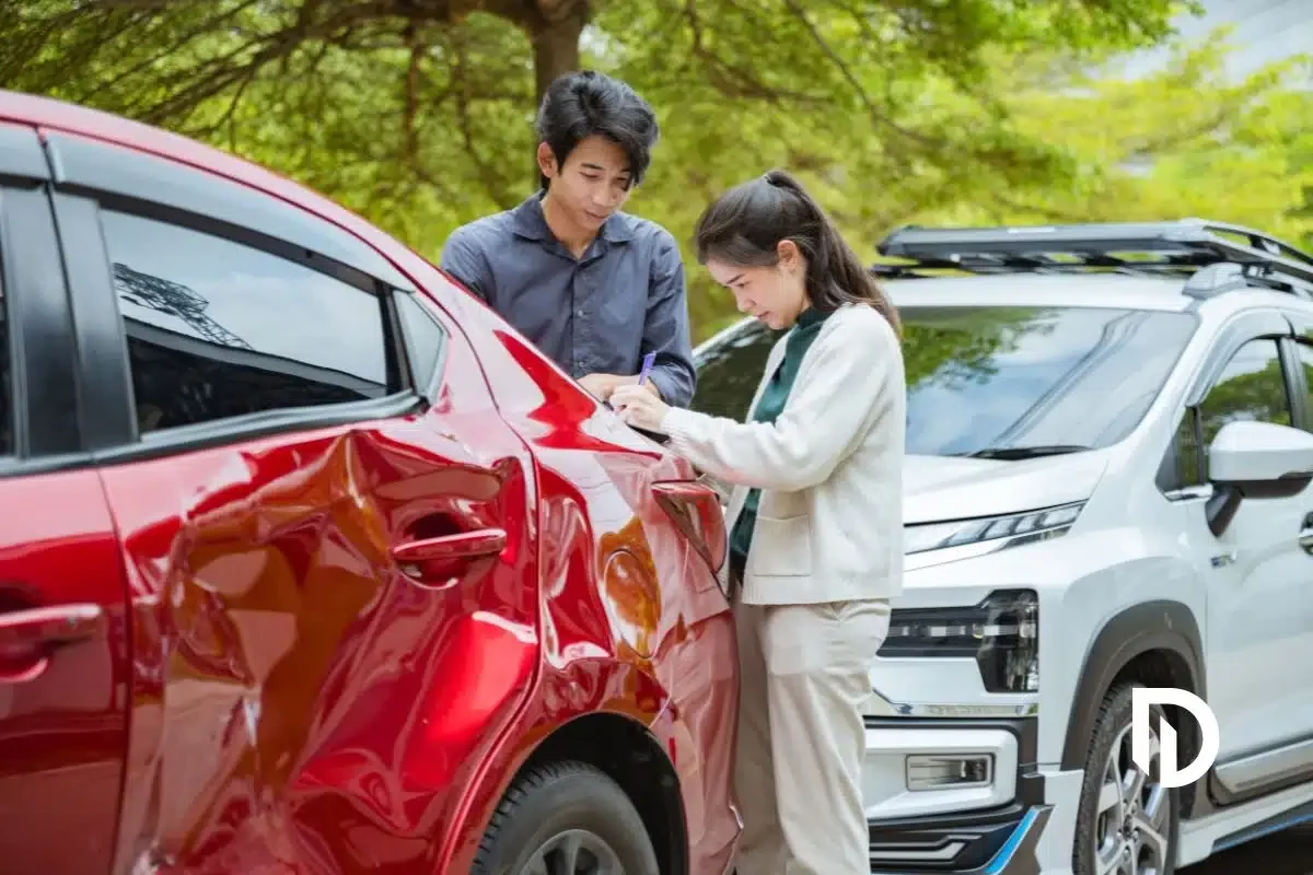 a man and a woman standing next to a red car with dens and damage after a collision